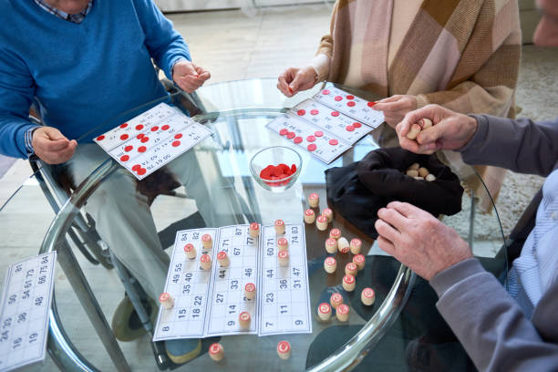 High angle close up of senior people playing lotto game sitting at glass table in living room